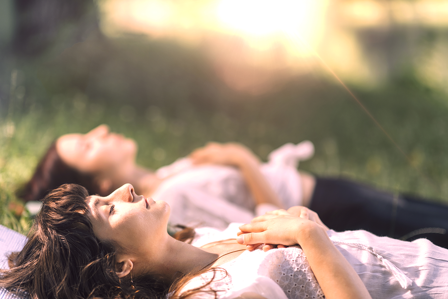 Two woman laying on grass with their eyes closed looking peaceful